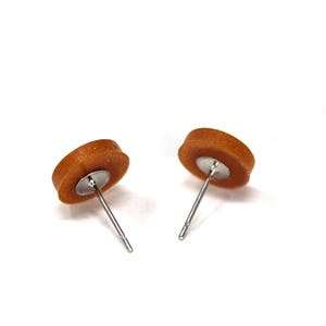 May include: A pair of brown stud earrings with silver posts. The earrings are round and have a slightly textured surface.