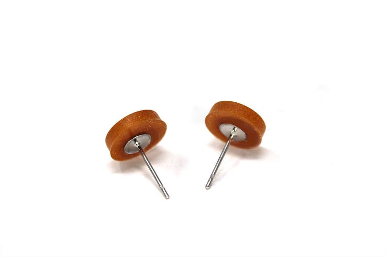 May include: A pair of brown stud earrings with silver posts. The earrings are round and have a slightly textured surface.