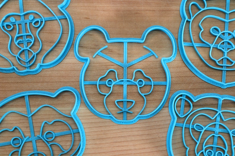 May include: Four blue plastic cookie cutters shaped like bear faces. Each cutter has a grid pattern on the face and a detailed outline of the bear's features.