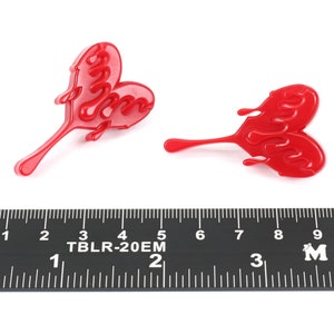 May include: Two red plastic heart-shaped charms with a dripping effect. The charms are approximately 5 cm long and are shown next to a ruler.