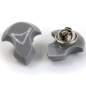 Puede incluir: Un pin de esmalte gris con un contorno blanco de la constelaci&oacute;n de Capricornio. El pin tiene un cierre de metal plateado en la parte posterior.