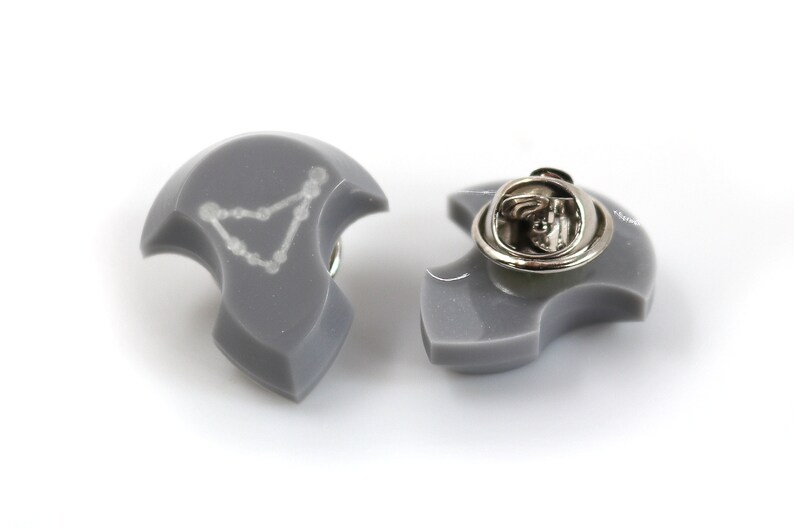 Puede incluir: Un pin de esmalte gris con un contorno blanco de la constelaci&oacute;n de Capricornio. El pin tiene un cierre de metal plateado en la parte posterior.