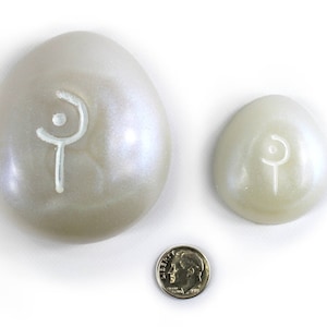 May include: Two white eggs with a white symbol on each. The larger egg is about the size of a US dime.