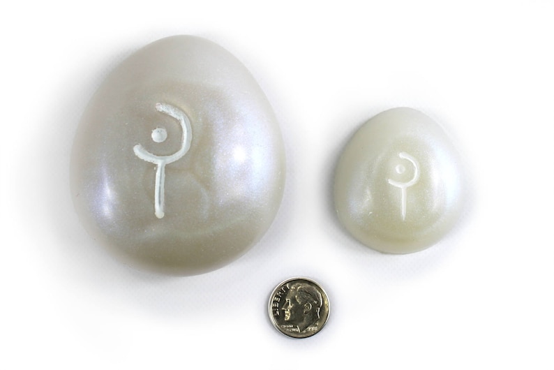 May include: Two white eggs with a white symbol on each. The larger egg is about the size of a US dime.