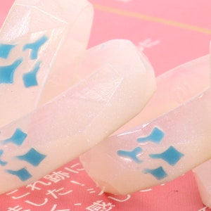 May include: Four white rings with a sparkly finish and blue geometric designs. The rings are stacked on top of each other.