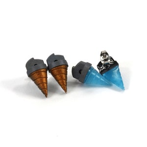 May include: Four unique stud earrings. Two pairs feature a cone design, one pair in a metallic bronze color and the other in a translucent blue. Each earring has a gray cap and a silver post.