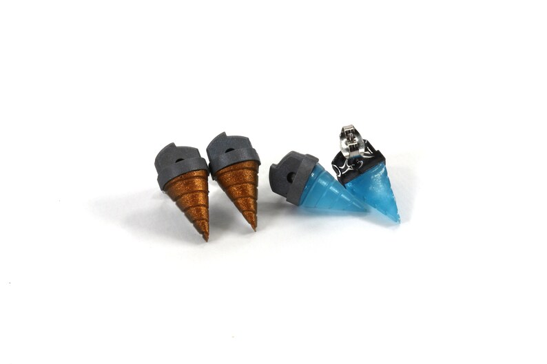 May include: Four unique stud earrings. Two pairs feature a cone design, one pair in a metallic bronze color and the other in a translucent blue. Each earring has a gray cap and a silver post.