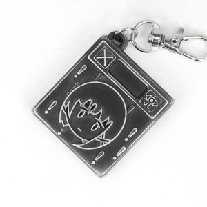May include: A silver-colored keychain featuring a cartoon character with a surprised expression. The keychain has a small digital display and a button with a plus sign. The keychain is attached to a silver-colored metal ring.