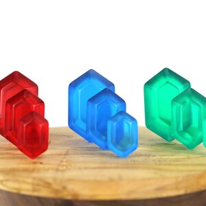 May include: A set of three stacks of colorful glass gems. The stacks are arranged in a row on a wooden surface. The gems are red, blue, and green.