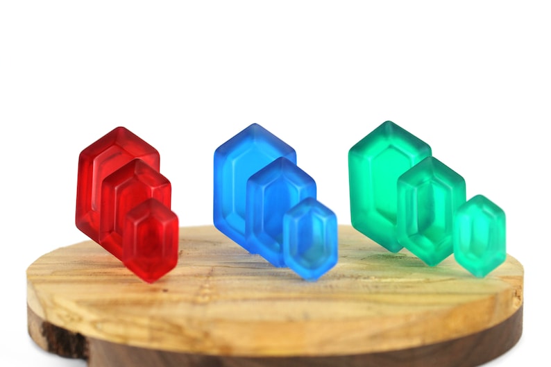 May include: A set of three stacks of colorful glass gems. The stacks are arranged in a row on a wooden surface. The gems are red, blue, and green.