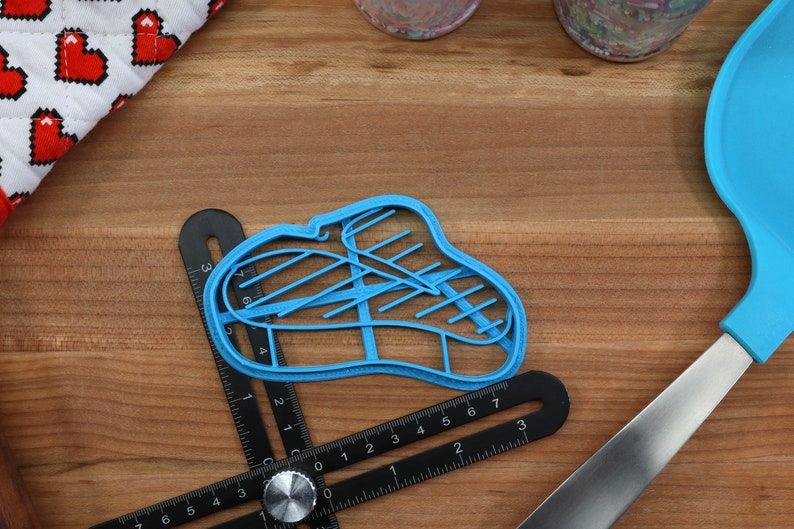 K&ouml;nnte beinhalten: Ein blauer Plastik-Ausstecher in Form eines Steaks mit Grillspuren. Der Ausstecher liegt auf einer Holzoberfl&auml;che mit einem Lineal und einem blauen Spatel.