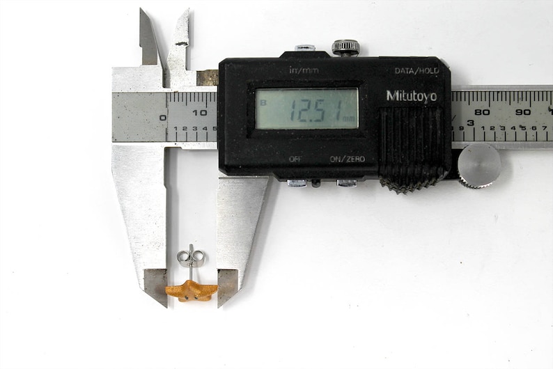 May include: A close-up of a silver caliper measuring a small, gold-colored starfish-shaped object. The caliper reads 12.51 mm.