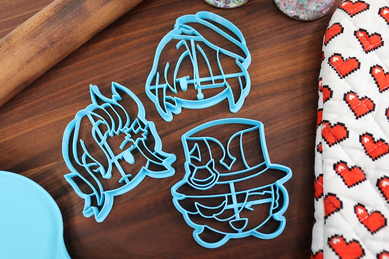 May include: Three blue plastic cookie cutters shaped like cartoon characters. The characters have large eyes, mouths, and hats.
