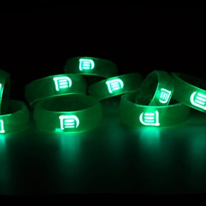 May include: A group of green glow-in-the-dark silicone rings with a white logo on each ring.