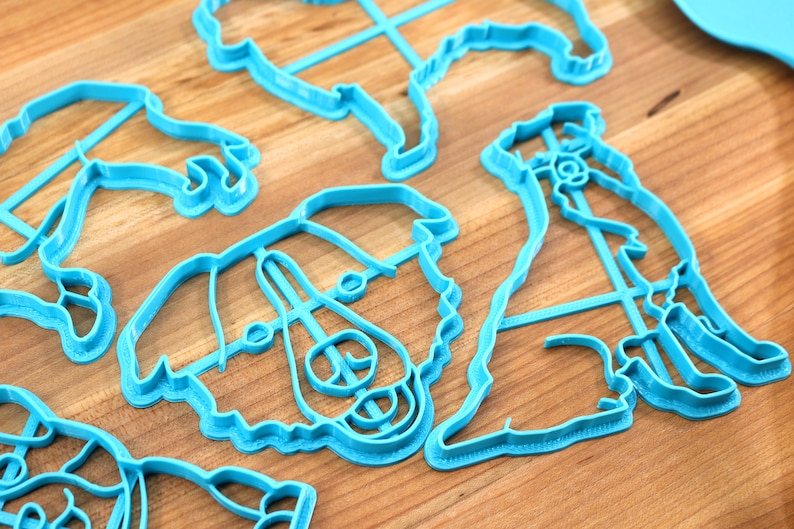 May include: A set of blue plastic cookie cutters shaped like dogs. The cutters are on a wooden surface.