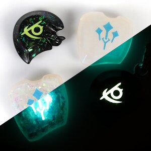 May include: Four resin charms, two with a blue and white design and two with a black and green design. The charms glow in the dark, with the blue and white charms glowing green and the black and green charms glowing white.
