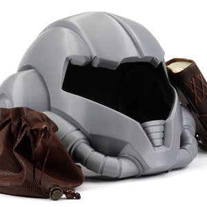 May include: A gray helmet with a brown leather pouch and a brown leather-bound book. The helmet has a futuristic design with a visor and a series of tubes.