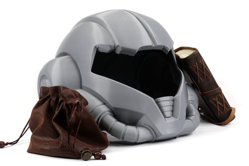 May include: A gray helmet with a brown leather pouch and a brown leather-bound book. The helmet has a futuristic design with a visor and a series of tubes.