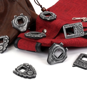 May include: A collection of eight silver-colored Digimon-style digital pet keychains. The keychains are scattered on a white surface, with two of them resting on a brown leather bag and a red fabric bag.