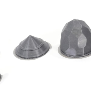 May include: Four grey 3D printed pieces with intricate designs. The pieces are shaped like cones and domes.