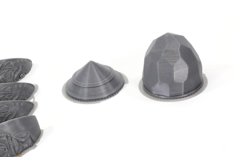 May include: Four grey 3D printed pieces with intricate designs. The pieces are shaped like cones and domes.