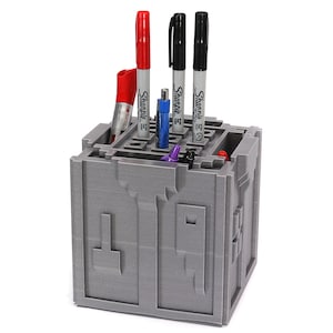 May include: A gray 3D printed pen holder shaped like a maze with black, red, and blue pens inside.