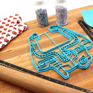 Peut inclure: Un emporte-pi&egrave;ce en plastique bleu en forme de manette de jeu vid&eacute;o sur une planche &agrave; d&eacute;couper en bois avec un rouleau &agrave; p&acirc;tisserie, une spatule et deux pots de vermicelles.