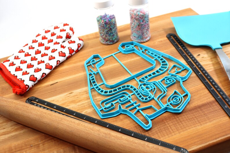 Peut inclure: Un emporte-pi&egrave;ce en plastique bleu en forme de manette de jeu vid&eacute;o sur une planche &agrave; d&eacute;couper en bois avec un rouleau &agrave; p&acirc;tisserie, une spatule et deux pots de vermicelles.