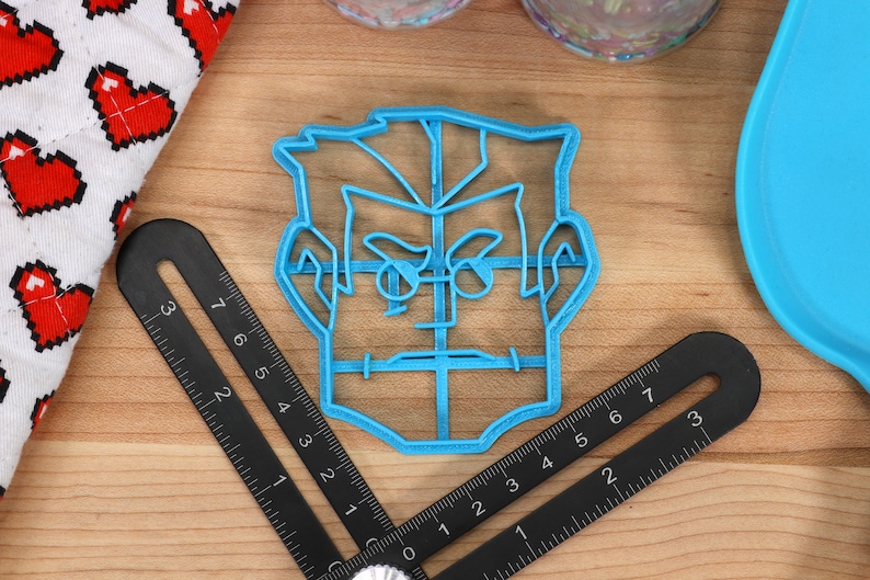 May include: A blue plastic cookie cutter shaped like a person's face with a serious expression. The cutter has a grid pattern on the face and hair.