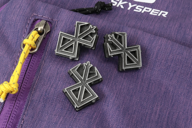 May include: Three silver-coloured metal pins with a geometric design. The pins are on a purple fabric background.