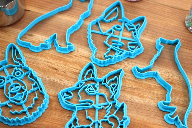 May include: Five blue plastic cookie cutters shaped like dogs. The cutters are on a wooden surface.