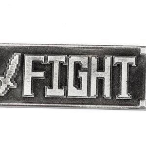 May include: A silver metal keychain with a pixelated sword and the word "FIGHT" in white lettering.