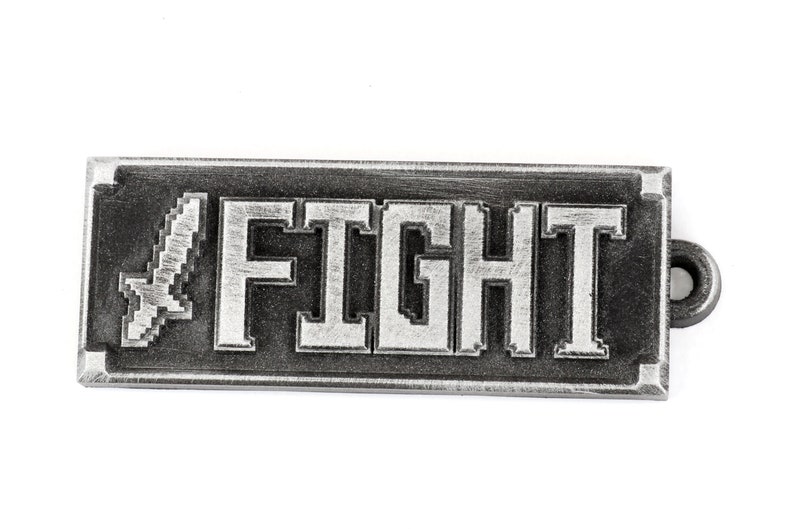 May include: A silver metal keychain with a pixelated sword and the word "FIGHT" in white lettering.