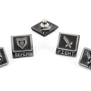 May include: Five silver-toned metal pins with pixelated graphics. The pins feature a sword, a shield, and the words "FIGHT" and "DEFEND".