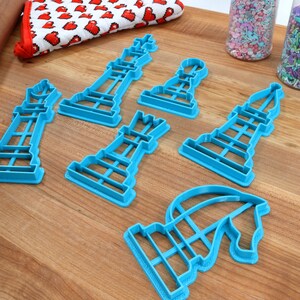 May include: A set of six blue plastic cookie cutters shaped like chess pieces. The pieces include a king, queen, bishop, rook, knight, and pawn.