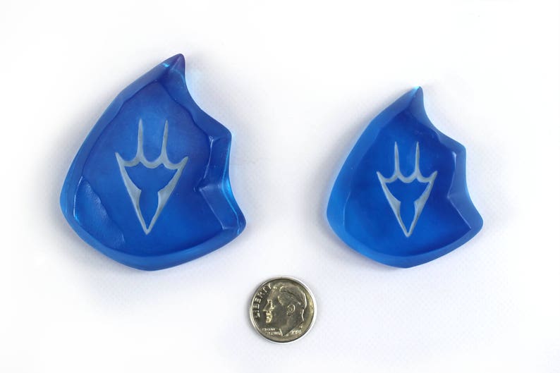May include: Two blue glass crystal-shaped pendants with a white stylized design. The pendants are about the size of a US dime.