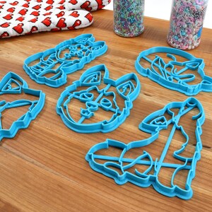 K&ouml;nnte beinhalten: F&uuml;nf blaue Plastik-Ausstecher in Form verschiedener Wolfsgesichter. Die Ausstecher liegen auf einer Holzoberfl&auml;che.