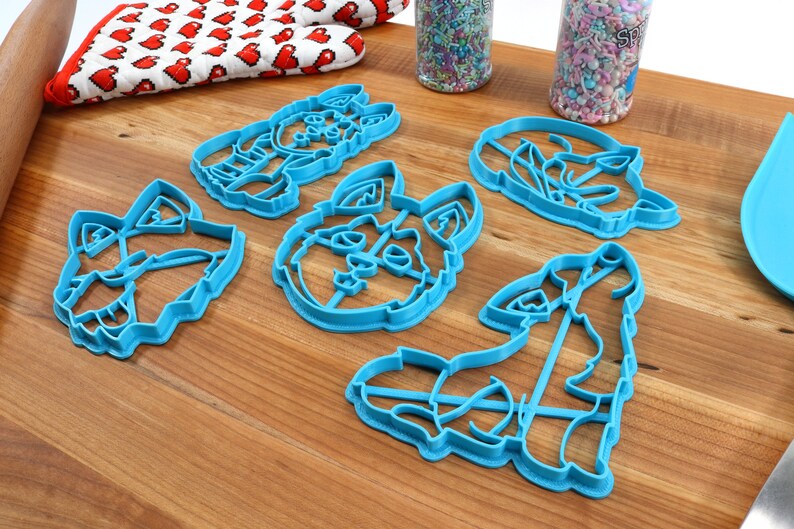 K&ouml;nnte beinhalten: F&uuml;nf blaue Plastik-Ausstecher in Form verschiedener Wolfsgesichter. Die Ausstecher liegen auf einer Holzoberfl&auml;che.