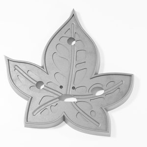 May include: A silver metal leaf-shaped ornament with a detailed design and five holes.