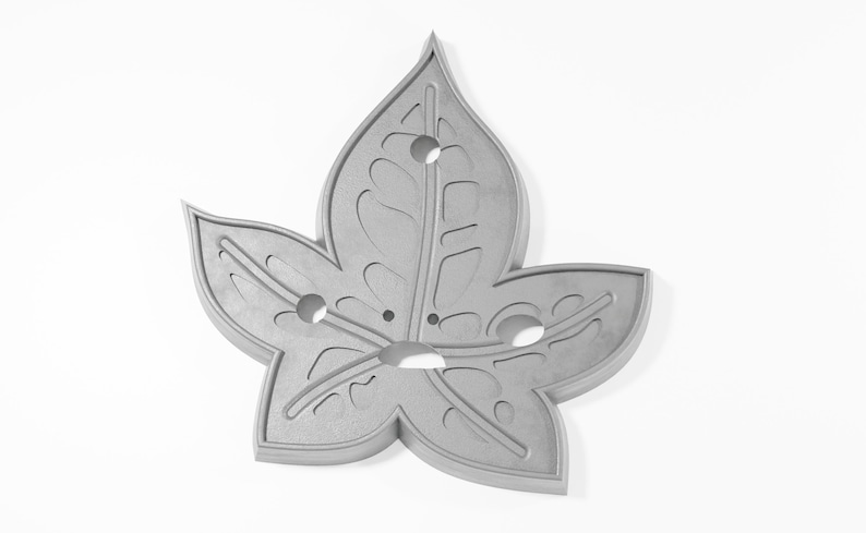 May include: A silver metal leaf-shaped ornament with a detailed design and five holes.