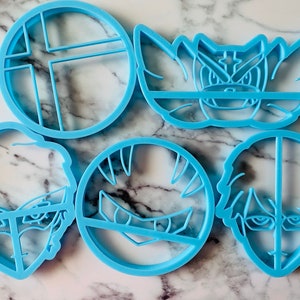 May include: Set of six blue plastic cookie cutters, featuring a video game character, a video game logo, and four different human faces.