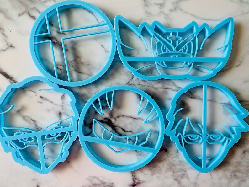 May include: Set of six blue plastic cookie cutters, featuring a video game character, a video game logo, and four different human faces.