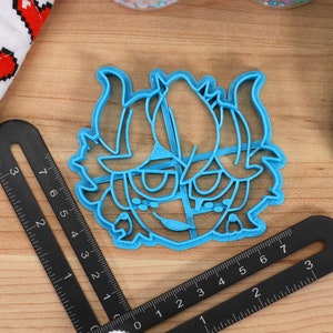 May include: A blue plastic cookie cutter shaped like a cartoon character with horns and a mischievous expression.