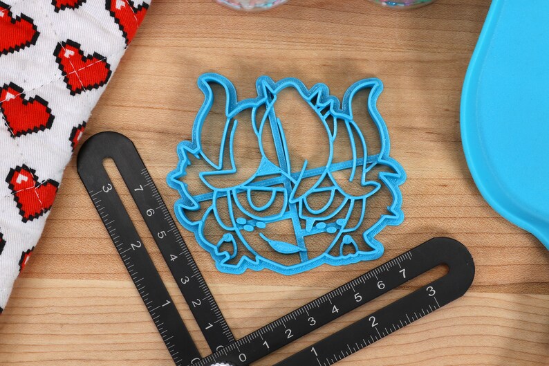 May include: A blue plastic cookie cutter shaped like a cartoon character with horns and a mischievous expression.