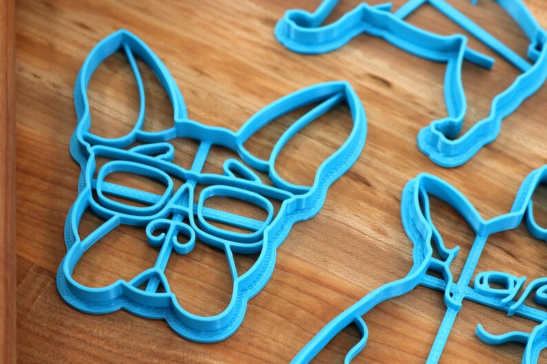 Puede incluir: Tres cortadores de galletas de pl&aacute;stico azul con forma de perro. El cortador del centro presenta un perro con gafas.