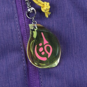 May include: A clear teardrop-shaped keychain with a pink symbol inside. The keychain is attached to a purple zipper on a bag.