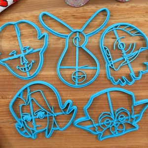 Pu&ograve; includere: Cinque tagliabiscotti in plastica blu a forma di personaggi dei cartoni animati. I tagliabiscotti sono su una superficie di legno.