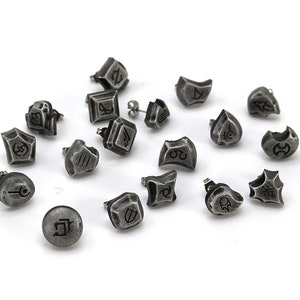 May include: A collection of 16 silver-toned earrings with various symbols and designs. The earrings are scattered on a white surface.