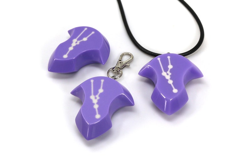 May include: Three purple pendants with a white constellation design. One pendant is on a black cord necklace, one is on a silver chain, and one is on a silver key chain.