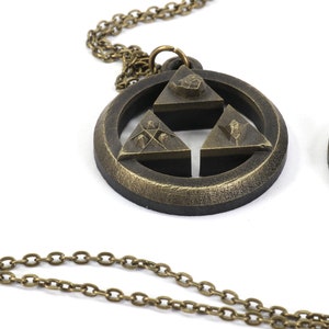 Puede incluir: Dos collares de color dorado con colgantes que representan el s&iacute;mbolo Triforce de la serie de videojuegos The Legend of Zelda. Cada colgante tiene un dise&ntilde;o circular con una estrella de tres puntas en el centro, con cada punta de la estrella representando un s&iacute;mbolo diferente.